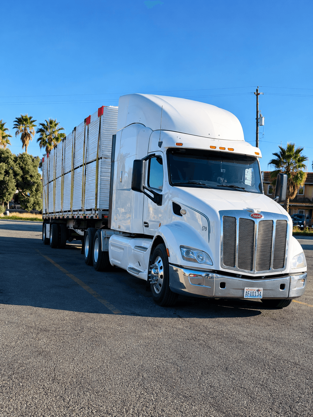White Peterbilt truck connected to a flatbed trailer loaded with strapped freight